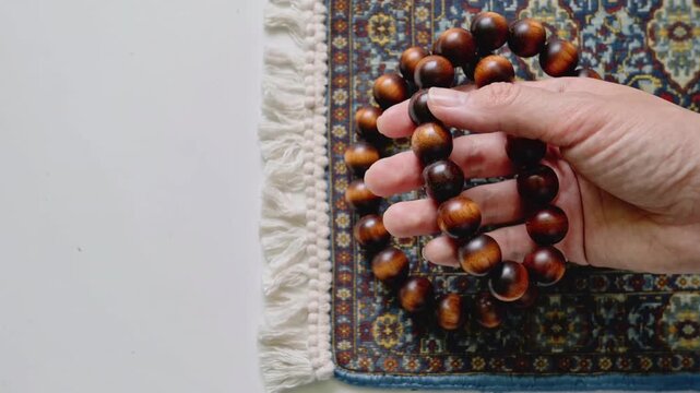 Hand holding wooden prayer beads over a small patterned rug rosary mala
