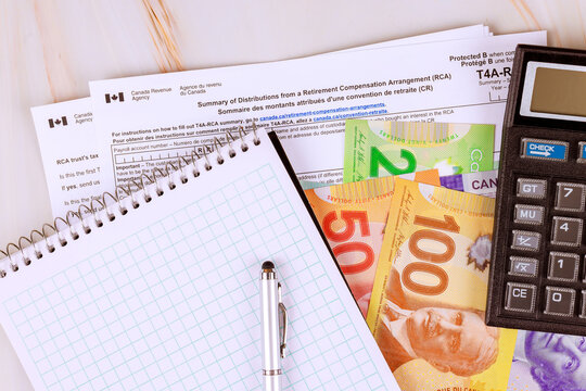 Review T4A tax forms, financial details using Canadian cash dollar money calculator on desk at home.