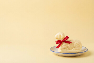 Traditional Easter butter lamb with red ribbon on ceramic plate over yellow background with copy space for religious greeting card or grocery store advertisement header