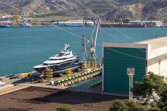 Port of Cartagena, Spain, showing the industrial shipyard and naval base with dry docks, cranes, workshops, and military ships. The port is a historic maritime hub on the Mediterranean coast