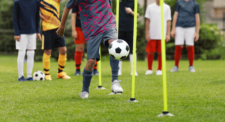 Obraz premium Youth Soccer Slalom Drill Training; Multiethnic Kids Practicing Ball Control with Poles on Grass Field