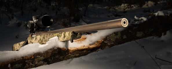Close-up of a bolt action rifle in a snowy treeline