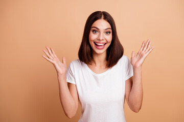 Bright smiling young woman with open hands wearing white tshirt against beige background