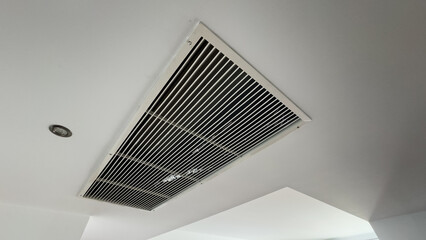 From bottom view of air conditioning wall mounted ventilation system on ceiling in white clean hotel guest room background. Hotel room air ventilation grill on the wall.