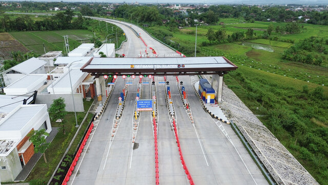 Aerial drone view highway with a toll booth or toll gate in the middle. The toll booth is surrounded by orange cones.