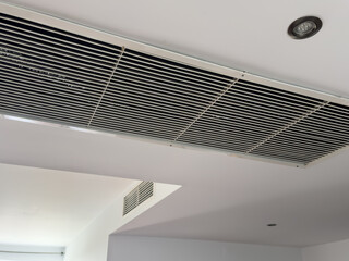 From bottom view of air conditioning wall mounted ventilation system on ceiling in white clean hotel guest room background. Hotel room air ventilation grill on the wall.