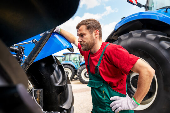 Professional mechanic inspecting farm equipment outdoors.