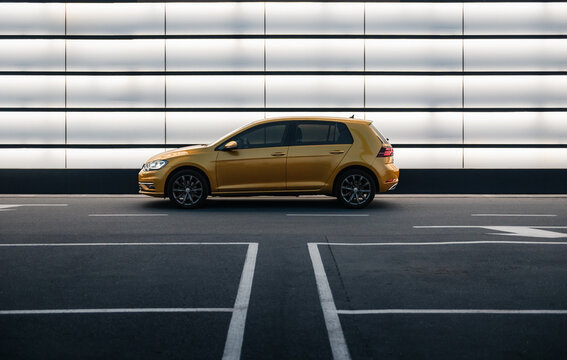 mustard yellow Volkswagen Golf in front of illuminated white wall at night. Side view of VW Golf mk7 - compact hatchback in parking lot. Kyiv, Ukraine - June 07 2025