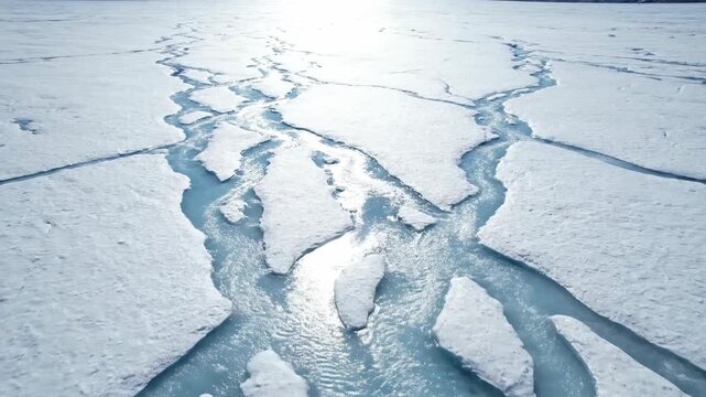 High angle aerial view of cracked ice sheets and blue water channels. Melting glacier patterns in the arctic. Global warming and environmental concept