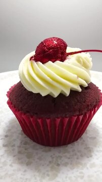 Vertical Close Up Video of Red Velvet Cupcake topped with Cream Cheese Frosting and Glitter-dusted Cherry