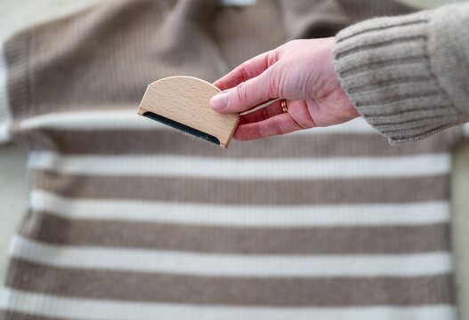 Wooden fabric lint brush in female hand cleaning sweater