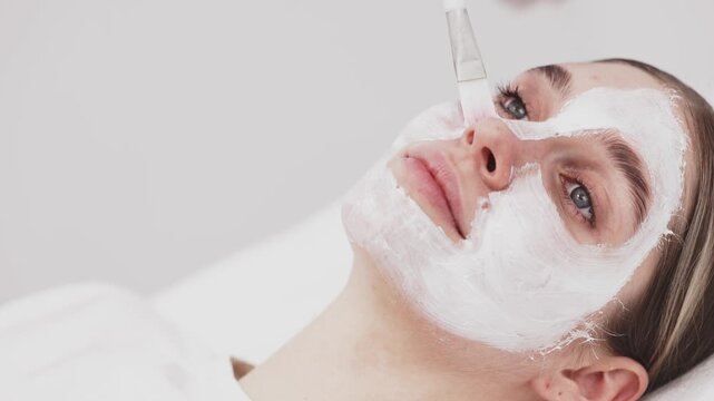 Professional facial treatment with female client. Beautician applies hydrating mask in blue gloves, skincare procedure, spa care and cosmetology concept.