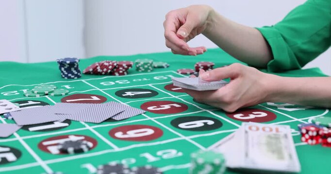 Casino dealer shuffles chips dealing cards on green table during game. Roulette layout shows bets and money near poker chips spread around speed up