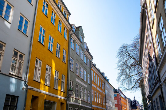 Urban street lined with colorful buildings and yellow facade presents architecture in copenhagen denmark as spring light makes shadows dance