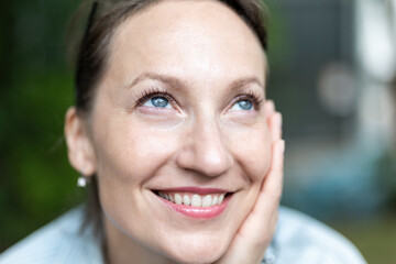 Naklejka premium Close-up detail portrait view young adult 40s beautiful smiling woman holding head chin with hand relaxed smiling sitting outdoors on day light. Female person close natural calm emotion outside