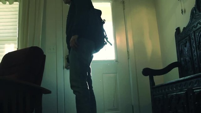 A young man in casual clothes and backpack opening the door and entering the house