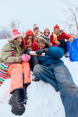 Happy friends sitting together and laughing in snowy landscape. Concept of carefree youth, friendship warmth, winter lifestyle scenes, social connection, and seasonal advertising visuals.
