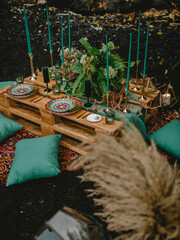 Boho outdoor table setting with plates, gold cutlery and candles on rustic pallets