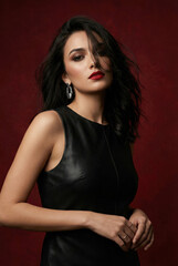Naklejka premium Elegant woman with dark hair and red lips wearing a black leather dress and statement earrings.
