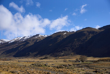 Andes mountains rising above the vast, arid patagonian steppe, creating a striking contrast between the rugged wilderness and the blue sky; roadtrip through Neuquen, Argentina.