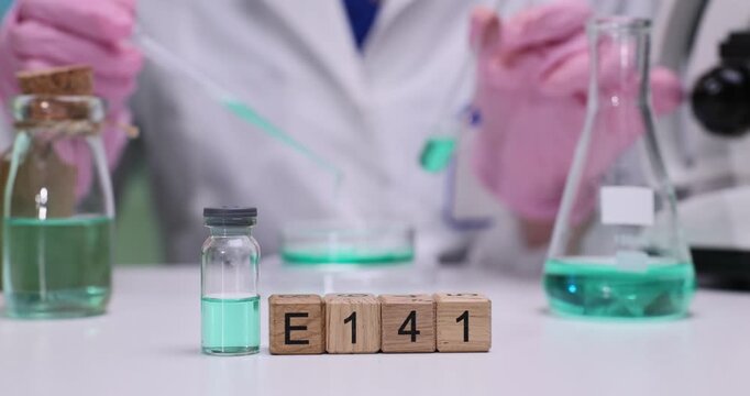 Wooden cubes spell code E141 near reagent samples. Scientist tests food colorant solution in laboratory glassware recording data during experiment