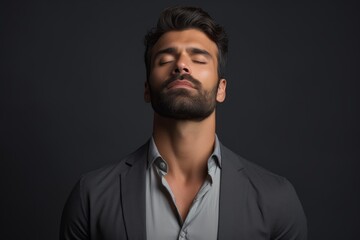 Obraz premium Man with beard closing eyes and meditating against a dark gray background