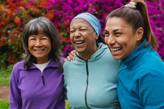 Happy multiracial senior women having fun together outdoor - Elderly generation people hugging each other at park