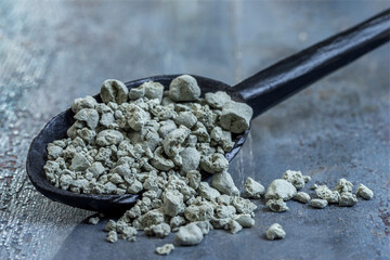 Grey Gravel Lies on a Black Spoon on a Table