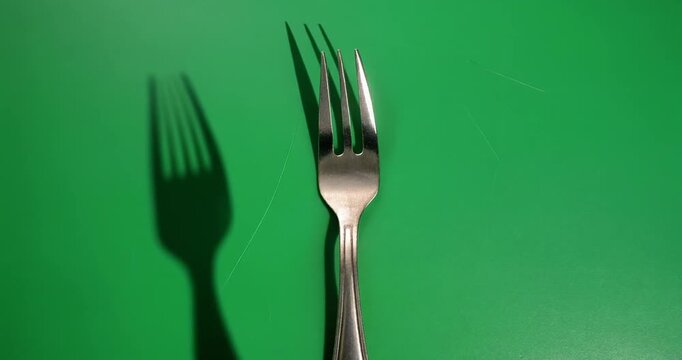 A silver fork stands upright on a green screen background casting a shadow.