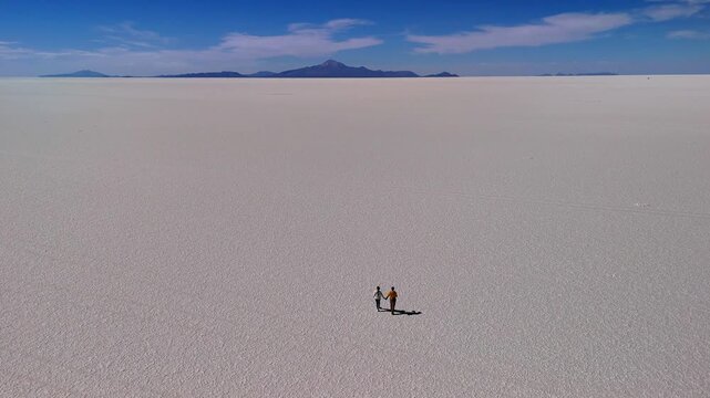Aerial drone video of a man and woman in Salar de Uyuni, Bolivia. The couple walks across the vast salt flat, enjoying the surrounding landscape.	