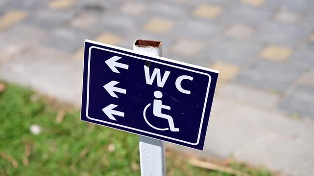 Close-up of sign with arrows pointing to restrooms and accessible areas, outside beach resort. Wheelchair-accessible sign is on blue background