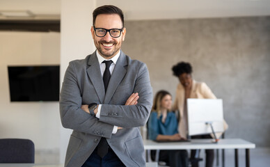 Handsome young business man standing confident in the corporate office in front of his team