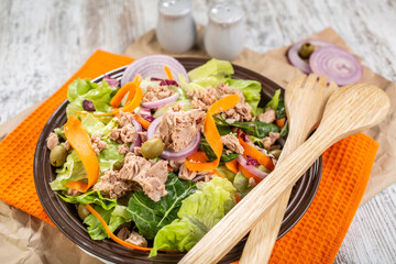 A plate of colorful salad with tuna, which includes lettuce, grated carrot, red onion, olives and tomatoes.