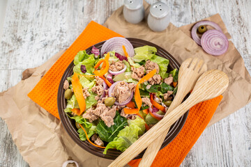 A plate of colorful salad with tuna, which includes lettuce, grated carrot, red onion, olives and tomatoes.