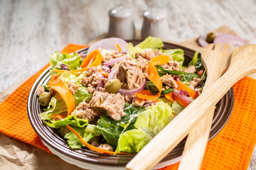 Bowl of colorful tuna salad with various vegetables and wooden serving utensils.