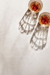 Transparent alcohol Glasses with dark shadows at sunlight on beige table, top view minimal lifestyle, aesthetic flat lay shiny glass sparkling at sun, summer strong drink, copyspace, vertical