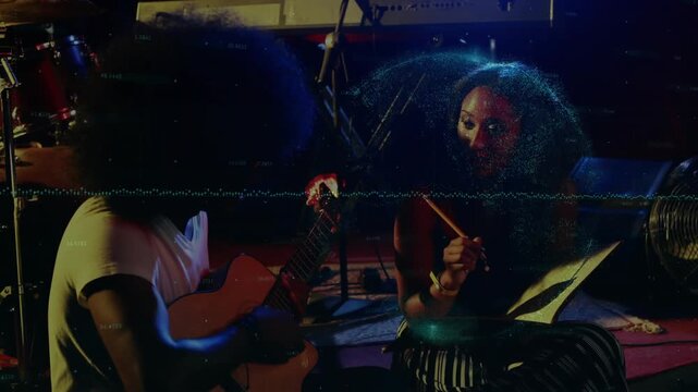 Guitarist starting to strum, female collaborator counting and tapping drum while writing song notes