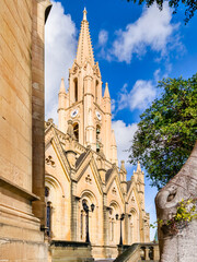 Parish Church with clock tower and stone facade under blue sky, Ghajnsielem, Gozo