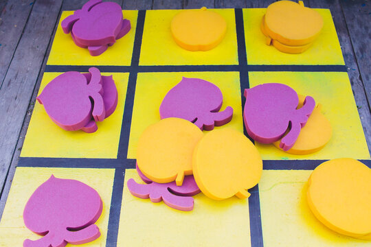 Vibrant foam fragments arranged on painted wooden tic tac toe surface. Assorted vivid foam shapes spread over painted wooden game board with shadows and texture