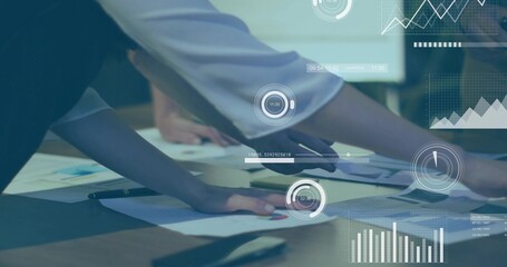 Leaning team reviewing reports at meeting table, with printed charts, digital overlays, in suits