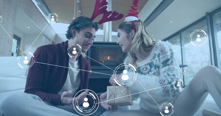 Naklejka premium Exchanging wrapped gift, two women sitting on rug in living room in antler headbands and sweaters