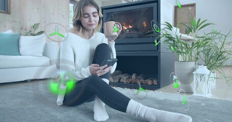 Naklejka premium Sitting woman holding smartphone, large mug by fireplace at home, in chunky sweater and jeans