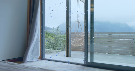 Framing sliding glass doors showing hanging rattan chair on wooden deck from bedroom, blue droplets