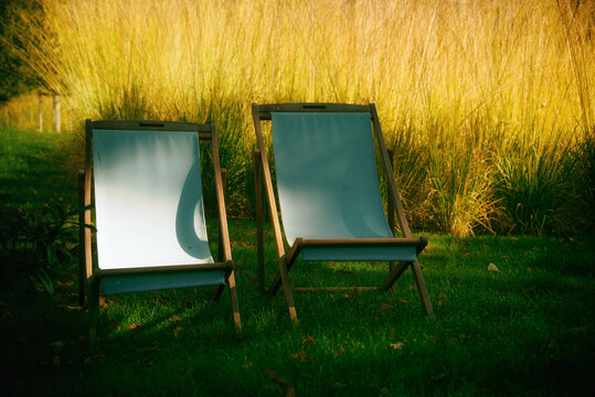 Two empty deck chairs side by side in a garden in the summer sunlight