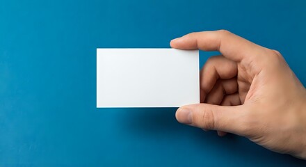 Fototapeta premium Hand holding blank white business card on blue background for corporate identity and branding mockup presentations.