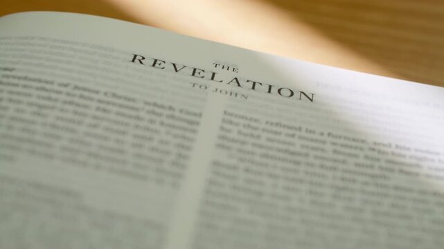 Bible pages flipping to Revelation book. Turning pages of the New Testament book regarding prophecy, the apocalypse, and the new kingdom. 4K close up shot for religious study and scripture.