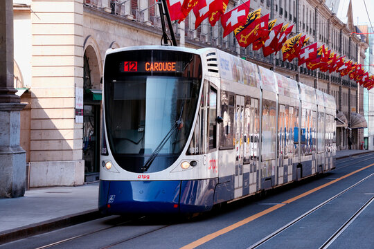 Geneva, Switzerland, Europe : Row of flags of Switzerland and flags of Geneva above street in historic part of the city, TPG tram on the road along Rue de la Corraterie