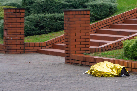 Golden emergency thermal blanket on pavement near brick stairs, accident or incident scene, medical rescue and emergency services, victim protection in urban area.
