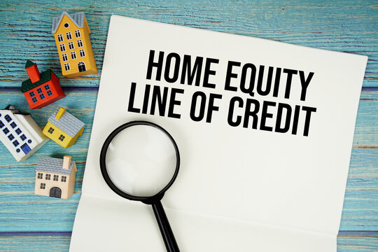 Notepad with "HELOC Home Equity Line Of Credit" with magnifying glass and house model on wooden background