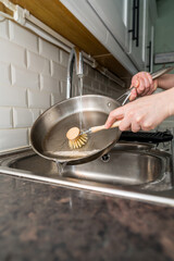 Woman washing dishes, frying pan with eco friendly wooden brush for sustainable lifestyle